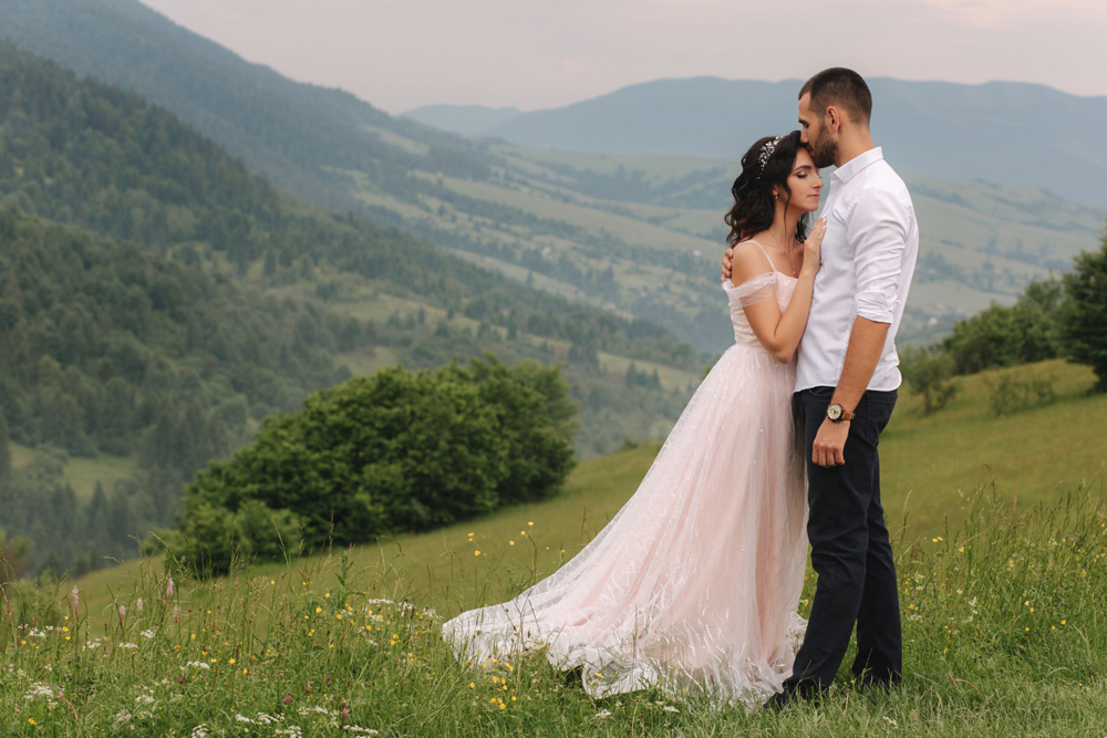 Beautiful young wedding couple standing on the green slope, hill. Groom and bride in Carpathian mountains